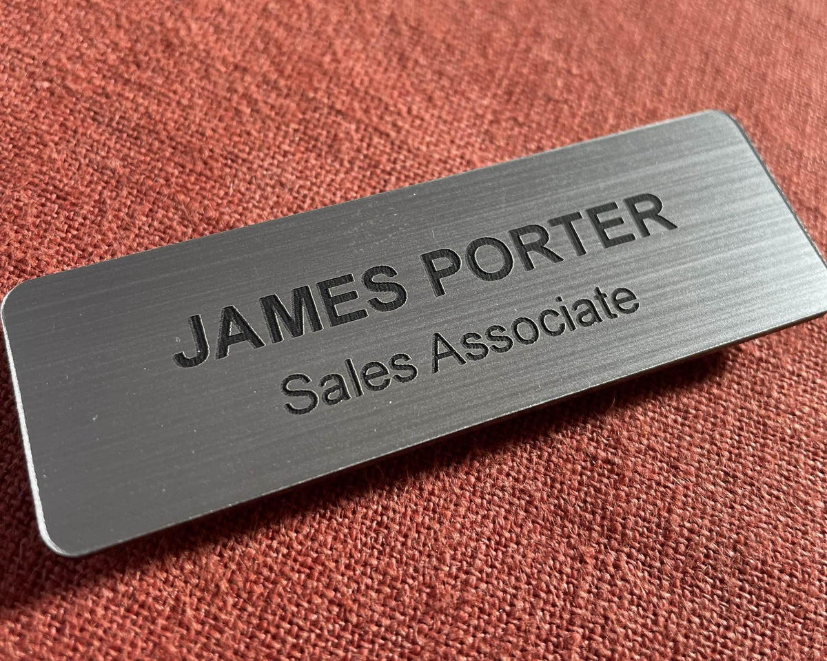 A brushed silver name badge with the name and title engraved in black.