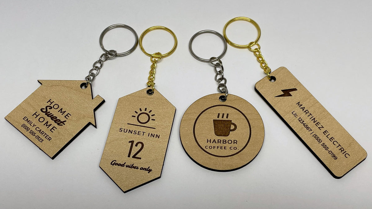 Four engraved maple keychains on gold and silver rings: a house shape for Emily Carter, a Sunset Inn room 12 tag, a round Harbor Coffee Co. logo and a Martinez Electric bar.