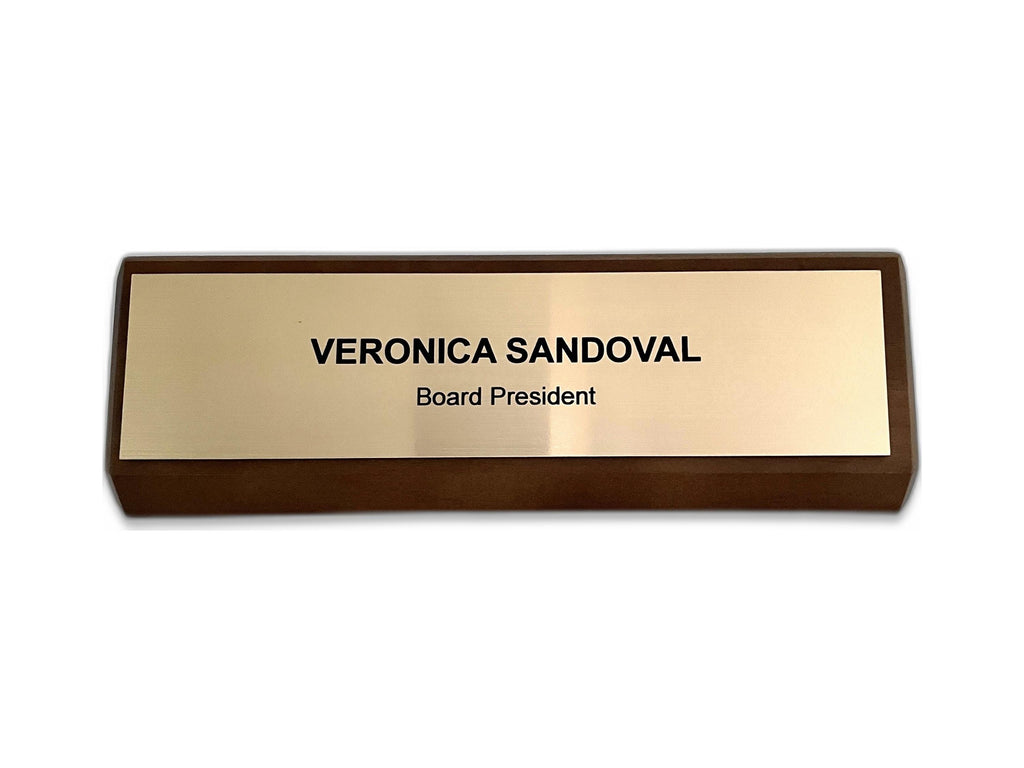 A rectangular desk nameplate featuring a dark walnut base and a gold-toned, metal-look plate. The text VERONICA SANDOVAL is engraved in black capital letters, with the title Board President below in smaller black text.