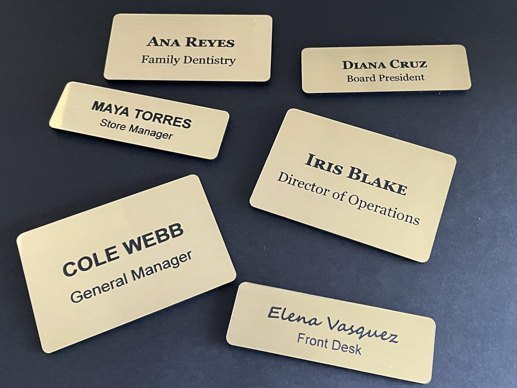 Six rectangular gold-toned name badges with rounded corners and black engraved text. The badges display names and titles including Ana Reyes, Diana Cruz, Maya Torres, Iris Blake, Cole Webb, and Elena Vasquez with their respective roles.