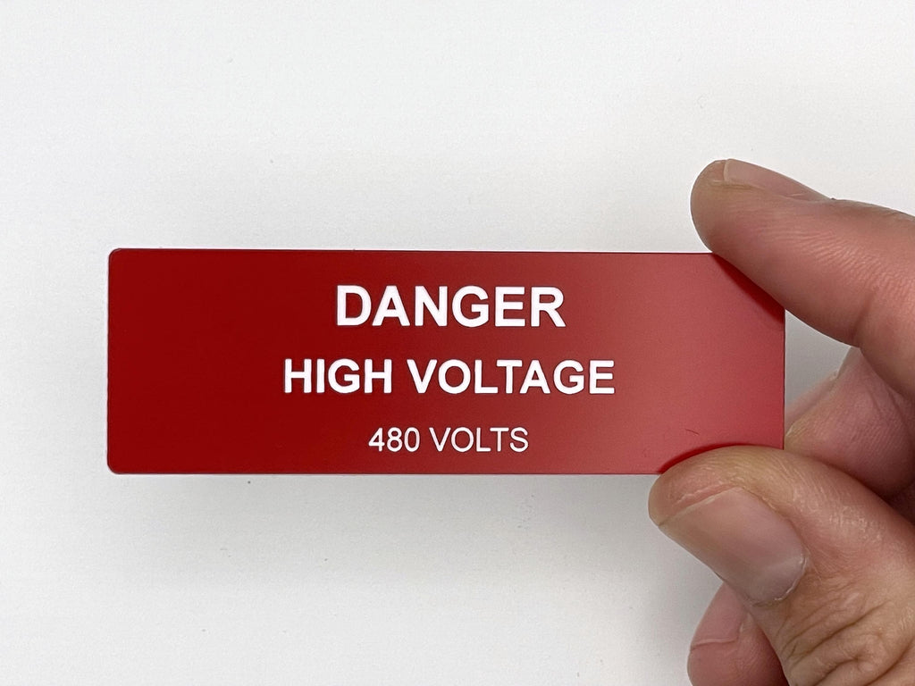A rectangular red safety sign with white text that reads DANGER HIGH VOLTAGE 480 VOLTS. The sign has a smooth, flat surface and is oriented horizontally, featuring bold, clear lettering for high visibility in industrial settings.