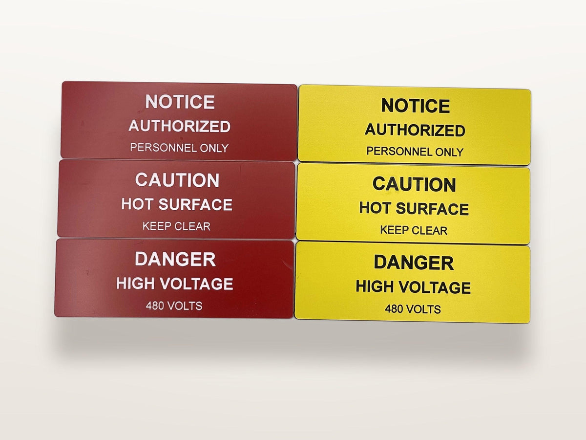 Six rectangular safety signs arranged in two columns. The left column features three dark red signs, while the right column features three yellow signs. Each sign displays black text: NOTICE AUTHORIZED PERSONNEL ONLY, CAUTION HOT SURFACE KEEP CLEAR, and DANGER HIGH VOLTAGE 480 VOLTS.