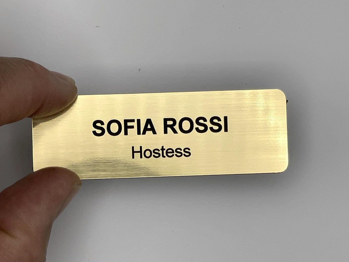 A rectangular gold-colored name badge with a brushed metal-look finish. The text SOFIA ROSSI is engraved in black capital letters on the top line, and the word Hostess is engraved in black letters on the line below.