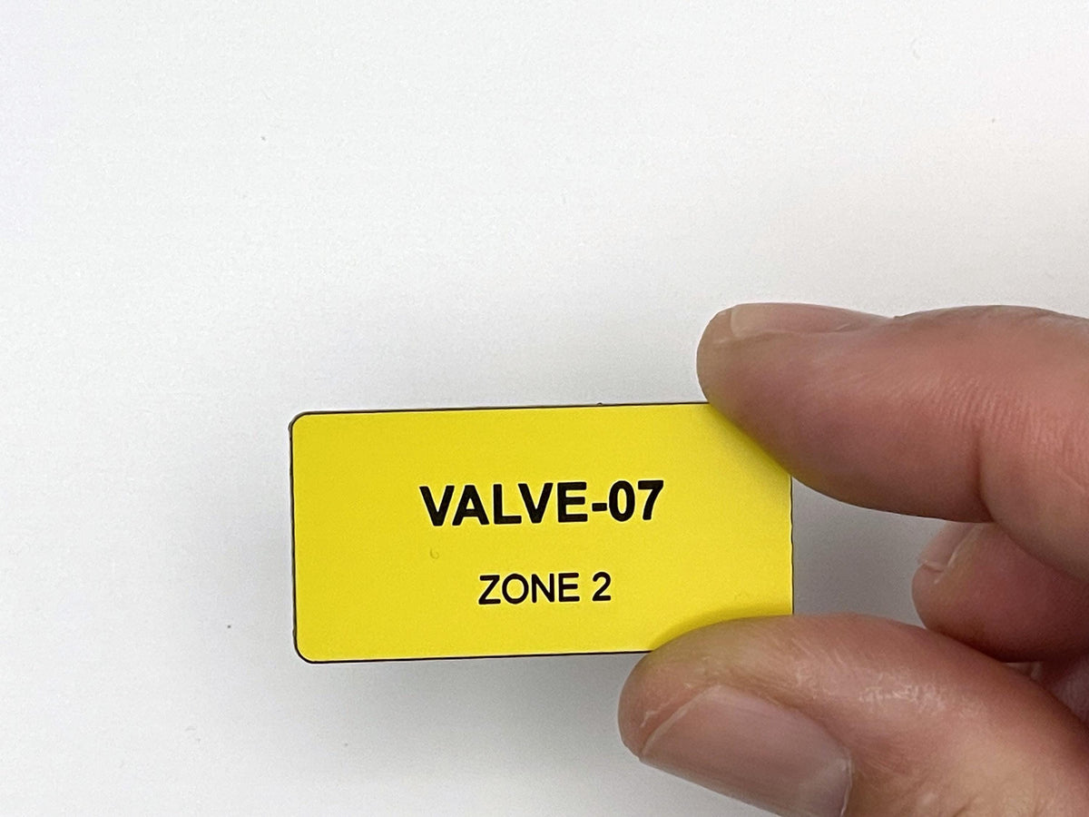 A rectangular yellow label with rounded corners featuring the black text VALVE-07 on the top line and ZONE 2 on the bottom line. The label has a smooth, matte finish and is designed for clear identification and organization purposes.