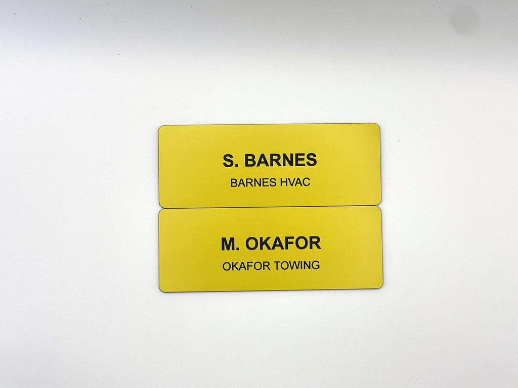 Two rectangular yellow name badges with rounded corners. The top badge features the black text S. BARNES and BARNES HVAC. The bottom badge features the black text M. OKAFOR and OKAFOR TOWING. Both badges have a smooth, solid finish.