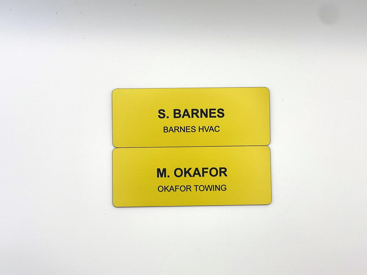 Two rectangular yellow name badges with rounded corners. The top badge features the black text S. BARNES and BARNES HVAC. The bottom badge features the black text M. OKAFOR and OKAFOR TOWING. Both badges have a smooth, solid finish.