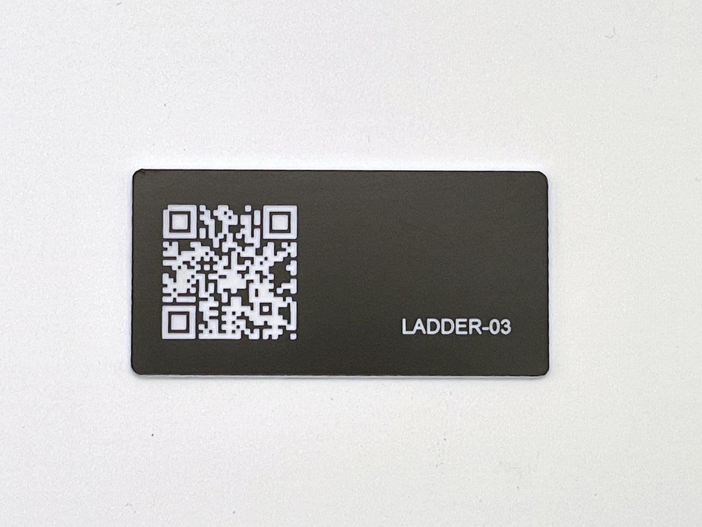 A rectangular black tag featuring a white QR code on the left side and the white text LADDER-03 engraved on the right side. The tag has a smooth, matte finish and rounded corners, presenting a clear contrast between the dark background and the white graphic elements.
