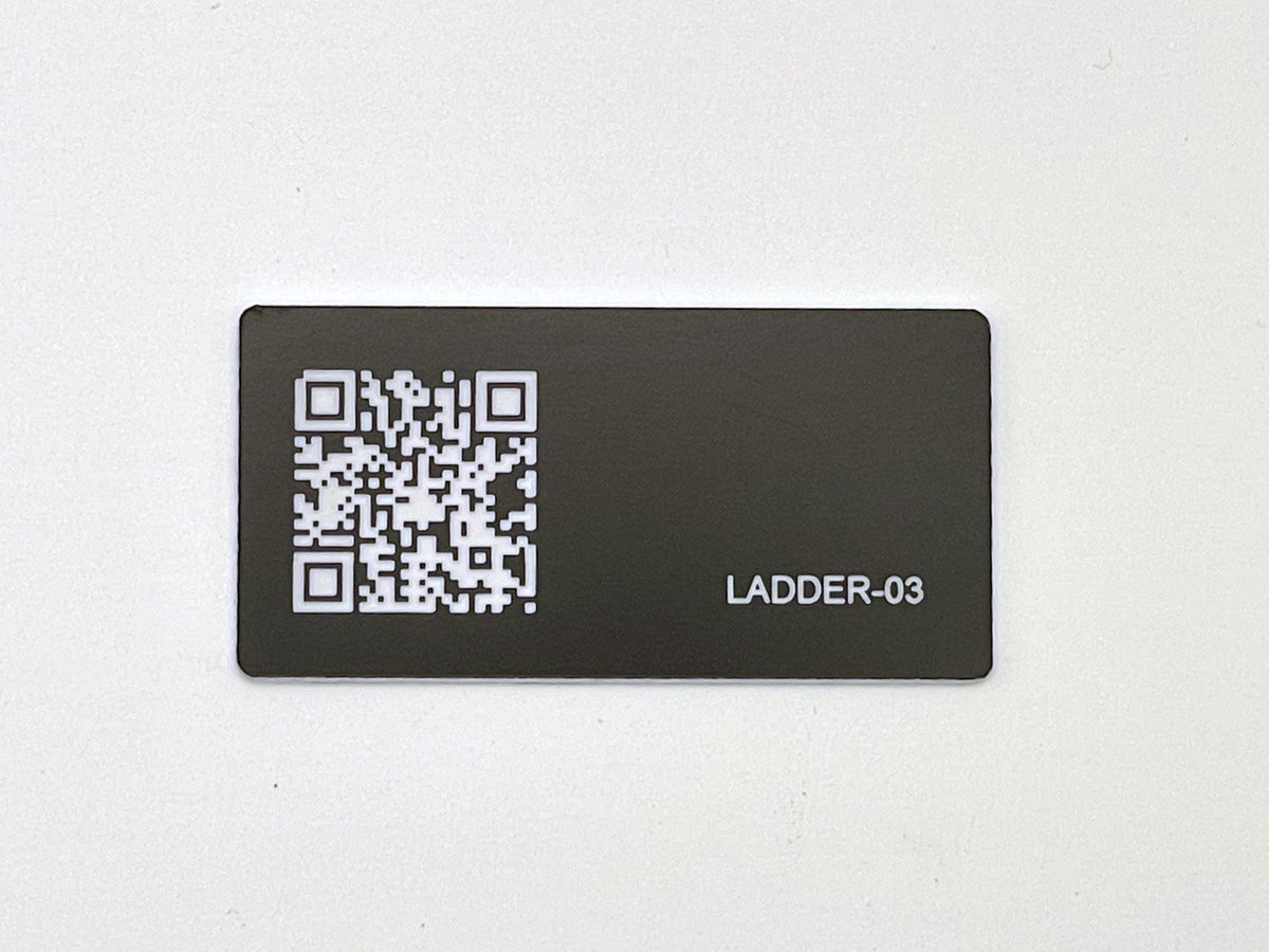 A rectangular black tag featuring a white QR code on the left side and the white text LADDER-03 engraved on the right side. The tag has a smooth, matte finish and rounded corners, presenting a clear contrast between the dark background and the white graphic elements.