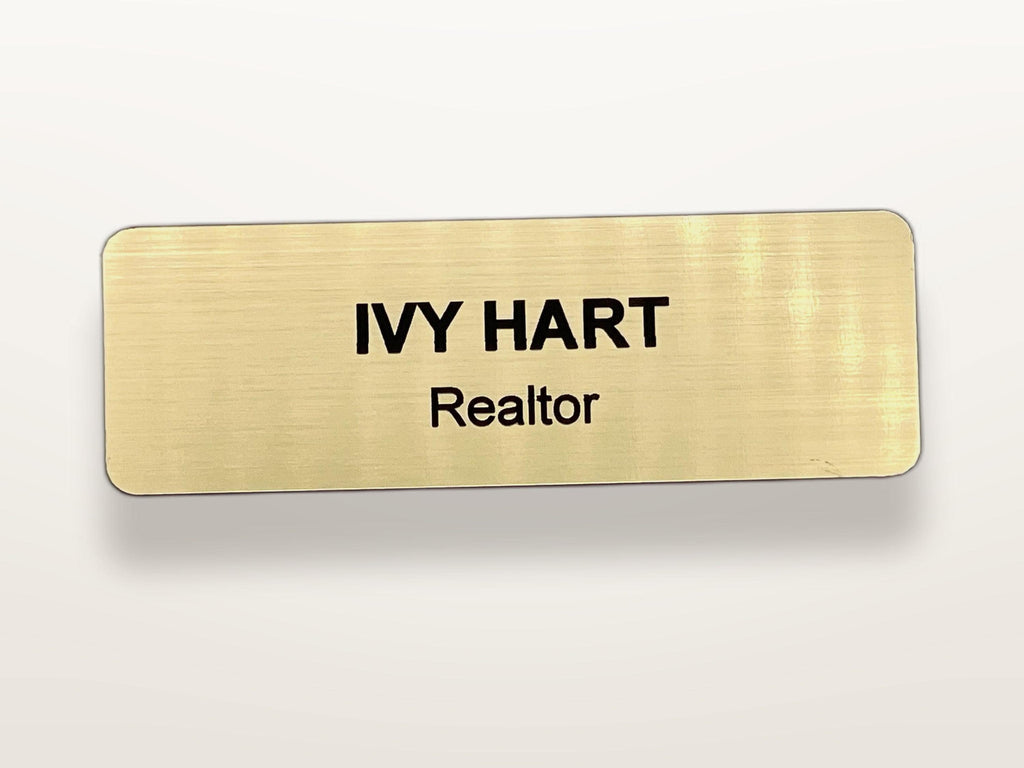 A rectangular name badge with a brushed gold finish and rounded corners. The text IVY HART is engraved in bold black capital letters on the top line, with the word Realtor engraved in smaller black letters on the line below.