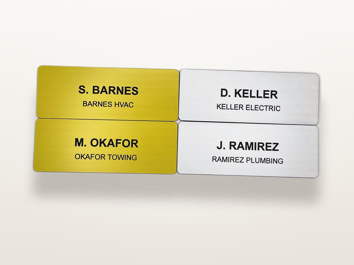Four rectangular name badges with rounded corners. Two are gold with black text reading S. BARNES BARNES HVAC and M. OKAFOR OKAFOR TOWING. Two are silver with black text reading D. KELLER KELLER ELECTRIC and J. RAMIREZ RAMIREZ PLUMBING.
