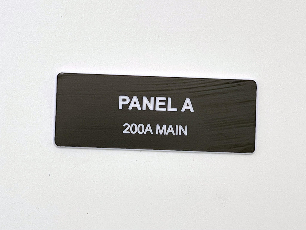 A rectangular black electrical panel label with a white border. The text engraved in white sans-serif font reads PANEL A on the top line and 200A MAIN on the bottom line. The surface of the label has a subtle horizontal wood grain texture.