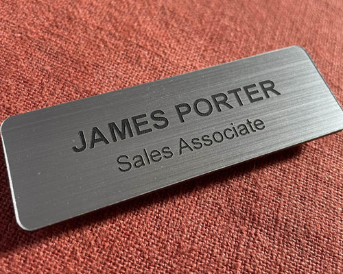 A rectangular brushed silver name badge featuring the engraved black text JAMES PORTER and Sales Associate.