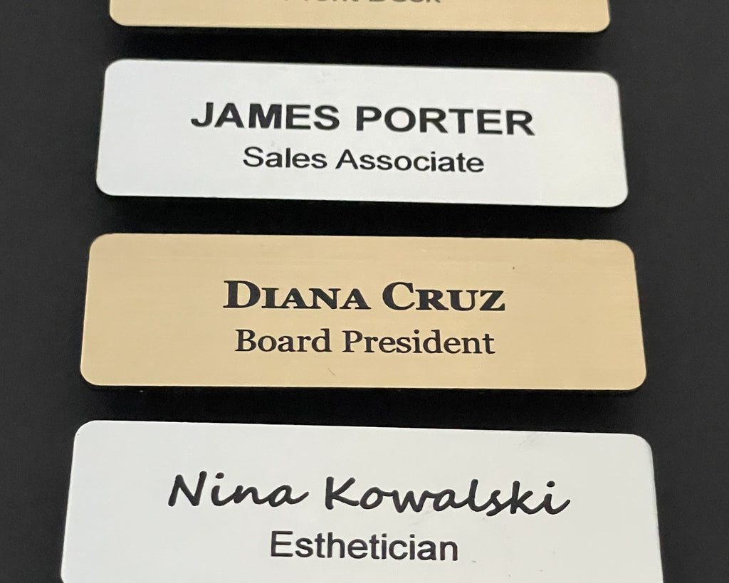 A collection of rectangular name badges featuring black text on white or gold metal-look backgrounds. The badges display names and job titles including James Porter, Diana Cruz, and Nina Kowalski.