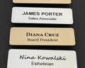 A collection of rectangular name badges featuring black text on white or gold metal-look backgrounds. The badges display names and job titles including James Porter, Diana Cruz, and Nina Kowalski.