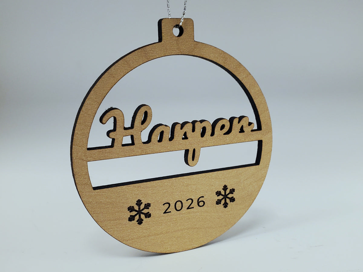 The Harper ornament at an angle on its silver string, showing the cut-through script name and the dark cut edges of the board.