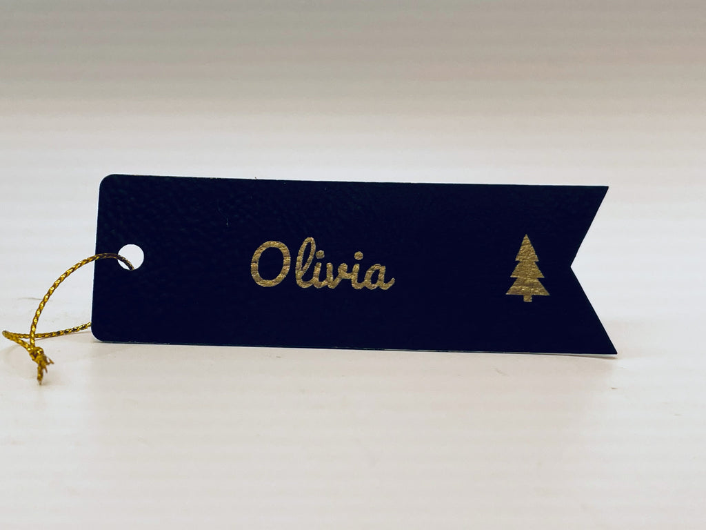 Black leatherette flag stocking tag engraved in gold: Olivia in script and a small tree, with gold string.