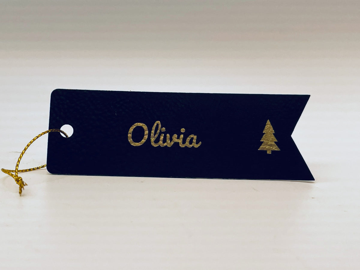 Black leatherette flag stocking tag engraved in gold: Olivia in script and a small tree, with gold string.