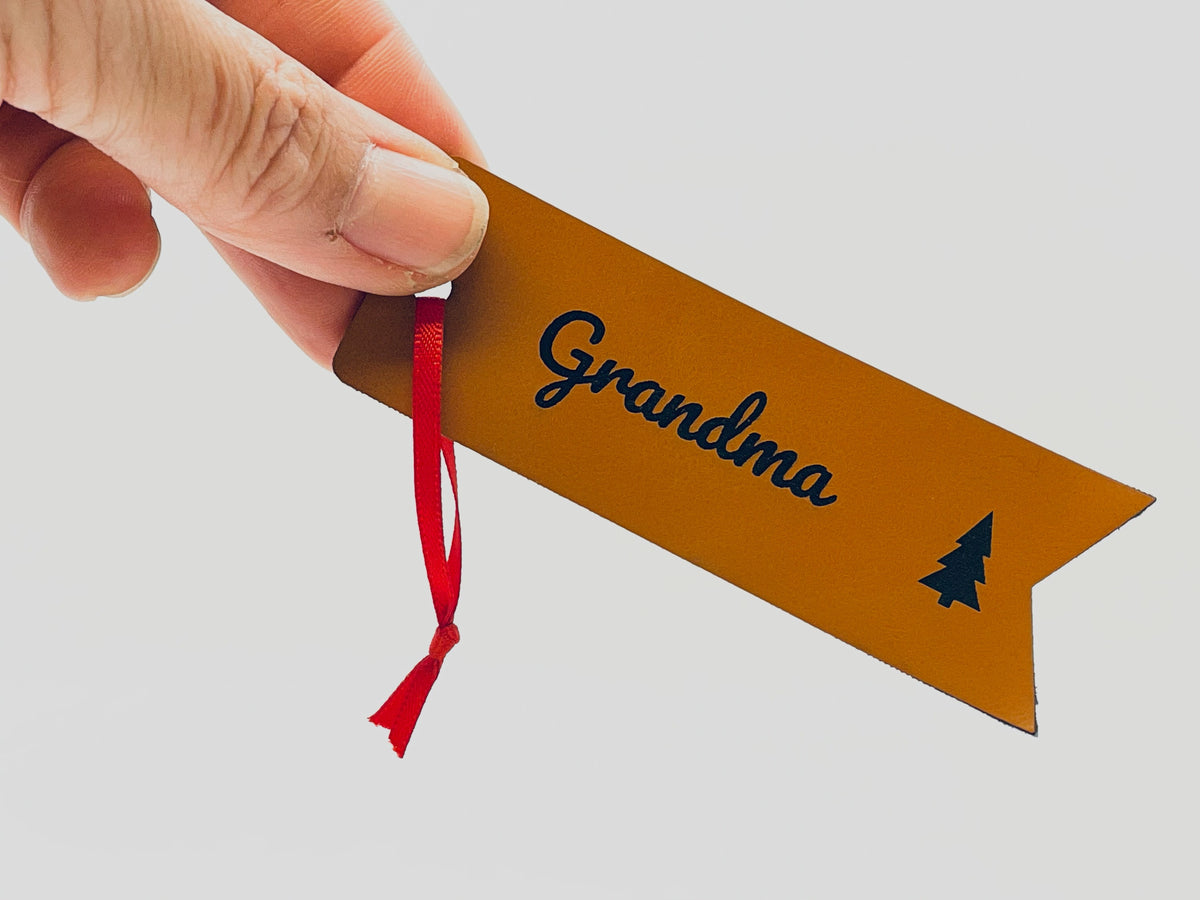 A hand holding the Grandma flag tag by its red ribbon, for size.
