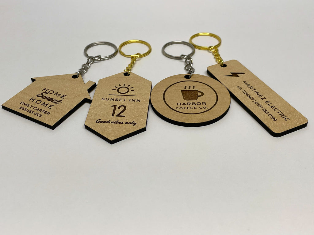 The four keychain shapes side by side on a table, house, motel tag, round and bar, in maple finish with silver and gold rings.