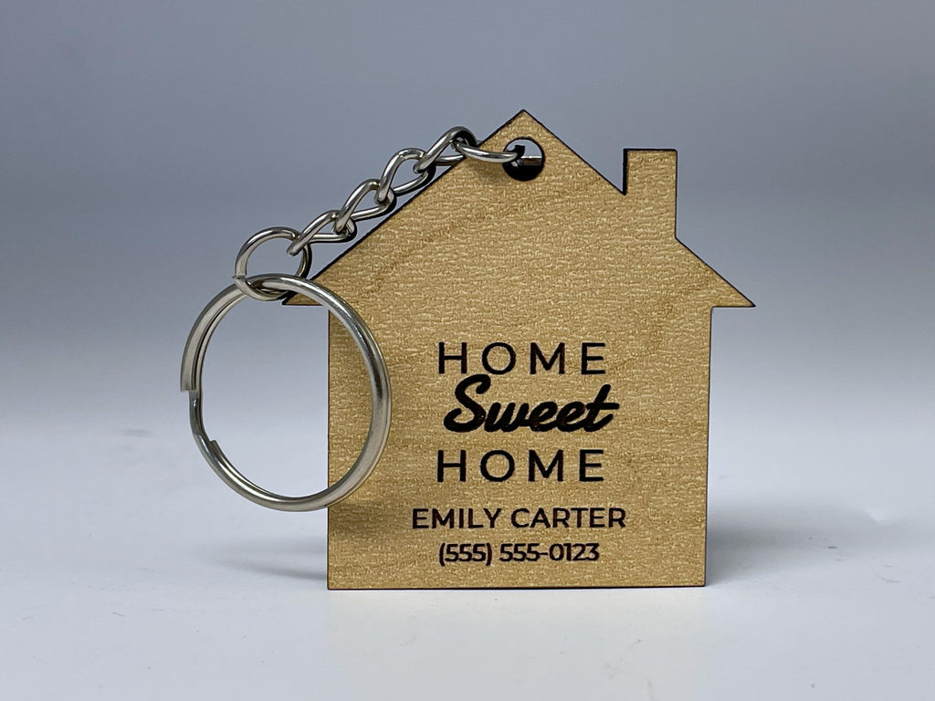 House shaped keychain in maple finish engraved HOME Sweet HOME, EMILY CARTER and a phone number, with a silver split ring and chain.