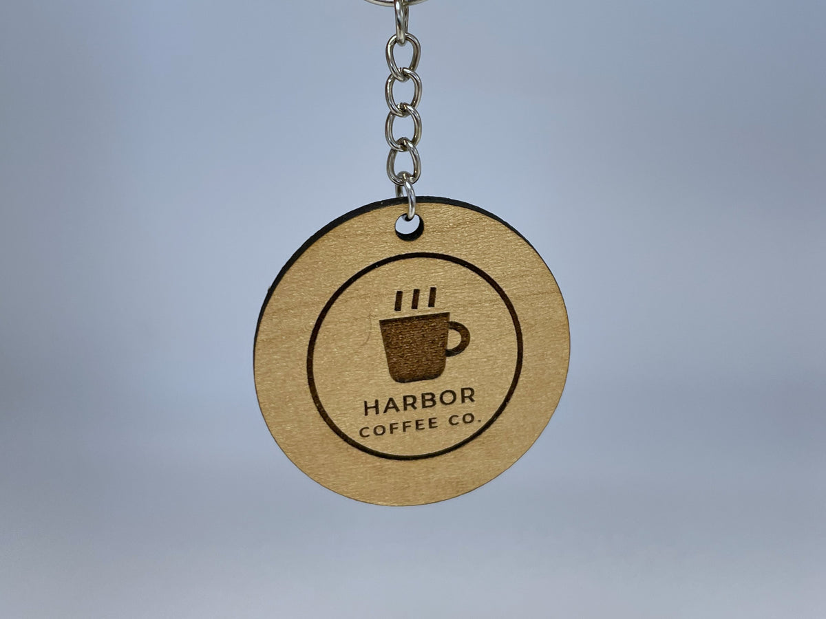 A round keychain in maple finish hanging from its silver chain, engraved with a coffee cup logo inside a border ring and HARBOR COFFEE CO.