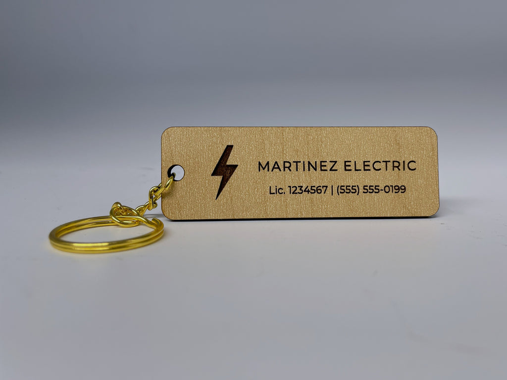 The bar keychain lying on a table with its gold split ring, engraved MARTINEZ ELECTRIC next to a lightning bolt.