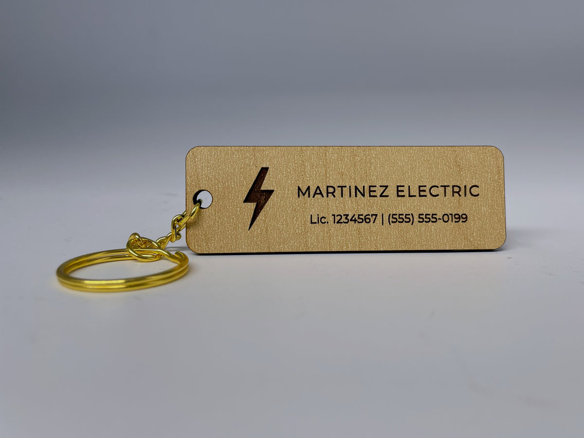 The bar keychain lying on a table with its gold split ring, engraved MARTINEZ ELECTRIC next to a lightning bolt.