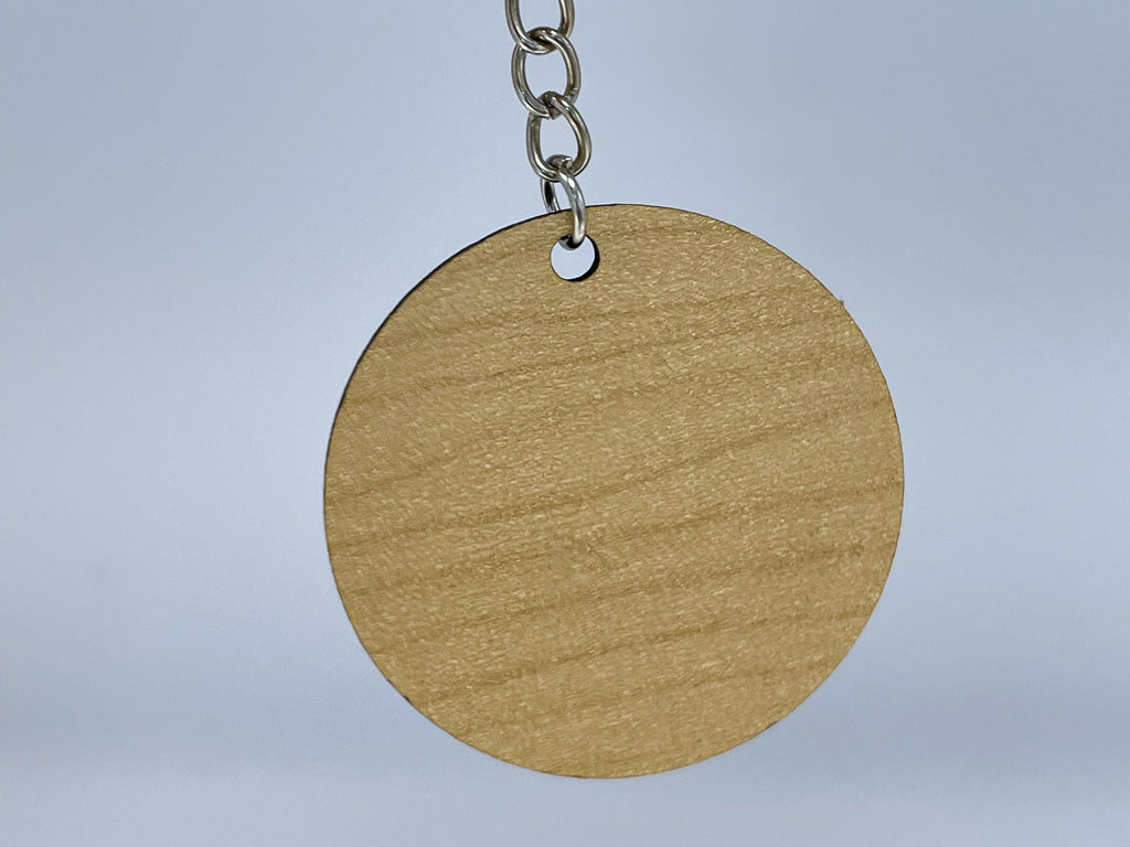 The plain back of the round keychain in maple finish, hanging from a silver chain.