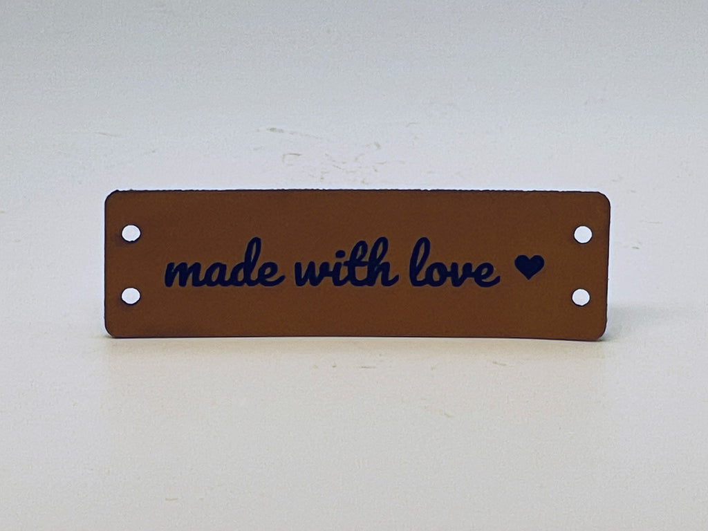 Rawhide leatherette label engraved made with love in script with a small heart, with two sewing holes at each end.