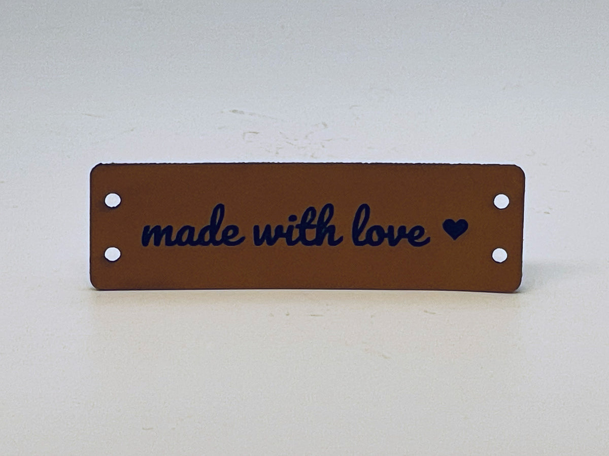Rawhide leatherette label engraved made with love in script with a small heart, with two sewing holes at each end.