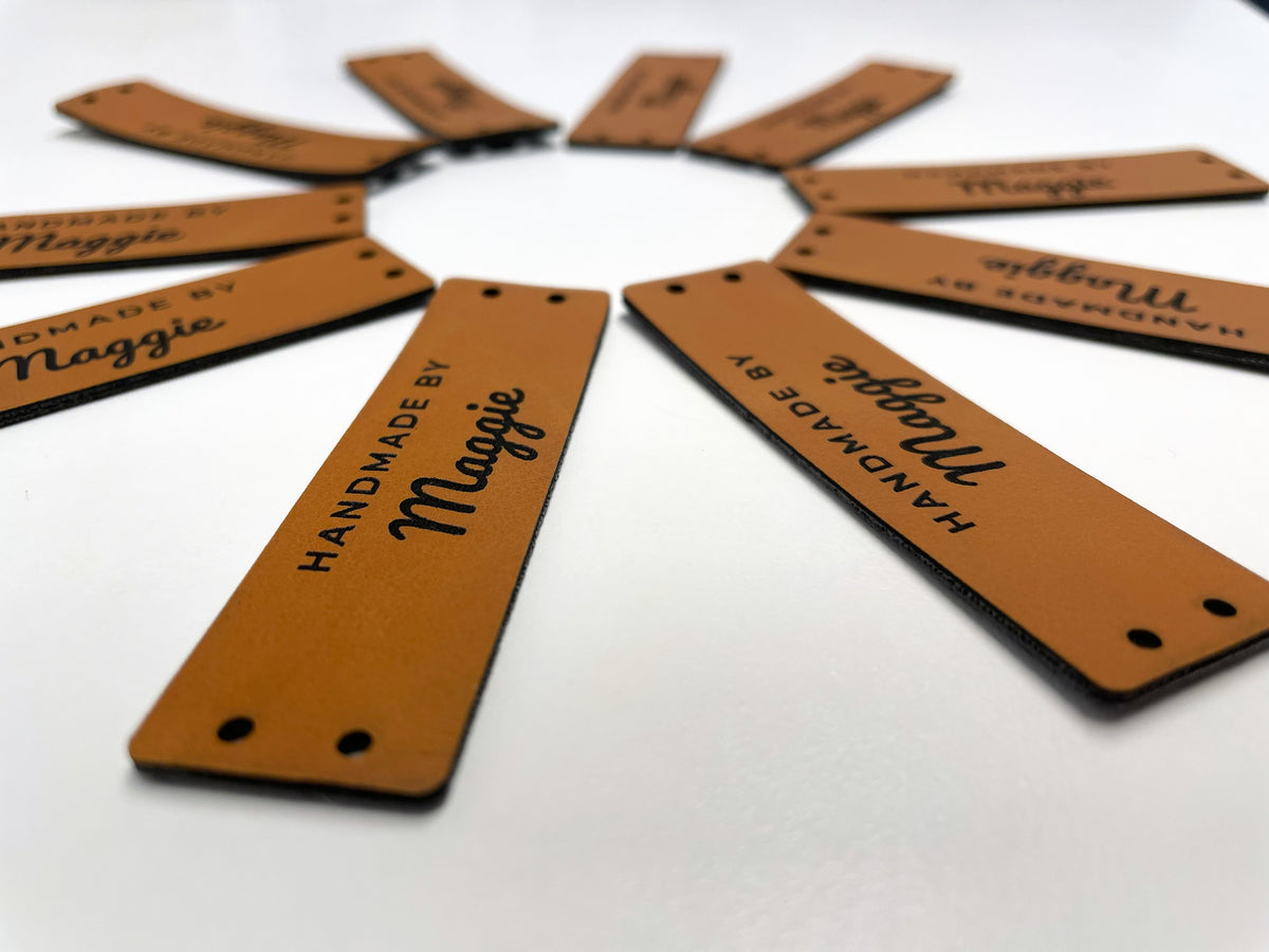 Rawhide leatherette HANDMADE BY Maggie labels laid out in a circle like a sunburst, seen from a low angle, the nearest label sharp.