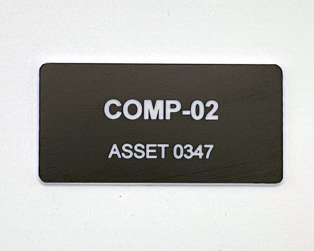 A rectangular black name tag with rounded corners featuring the white text COMP-02 and ASSET 0347.