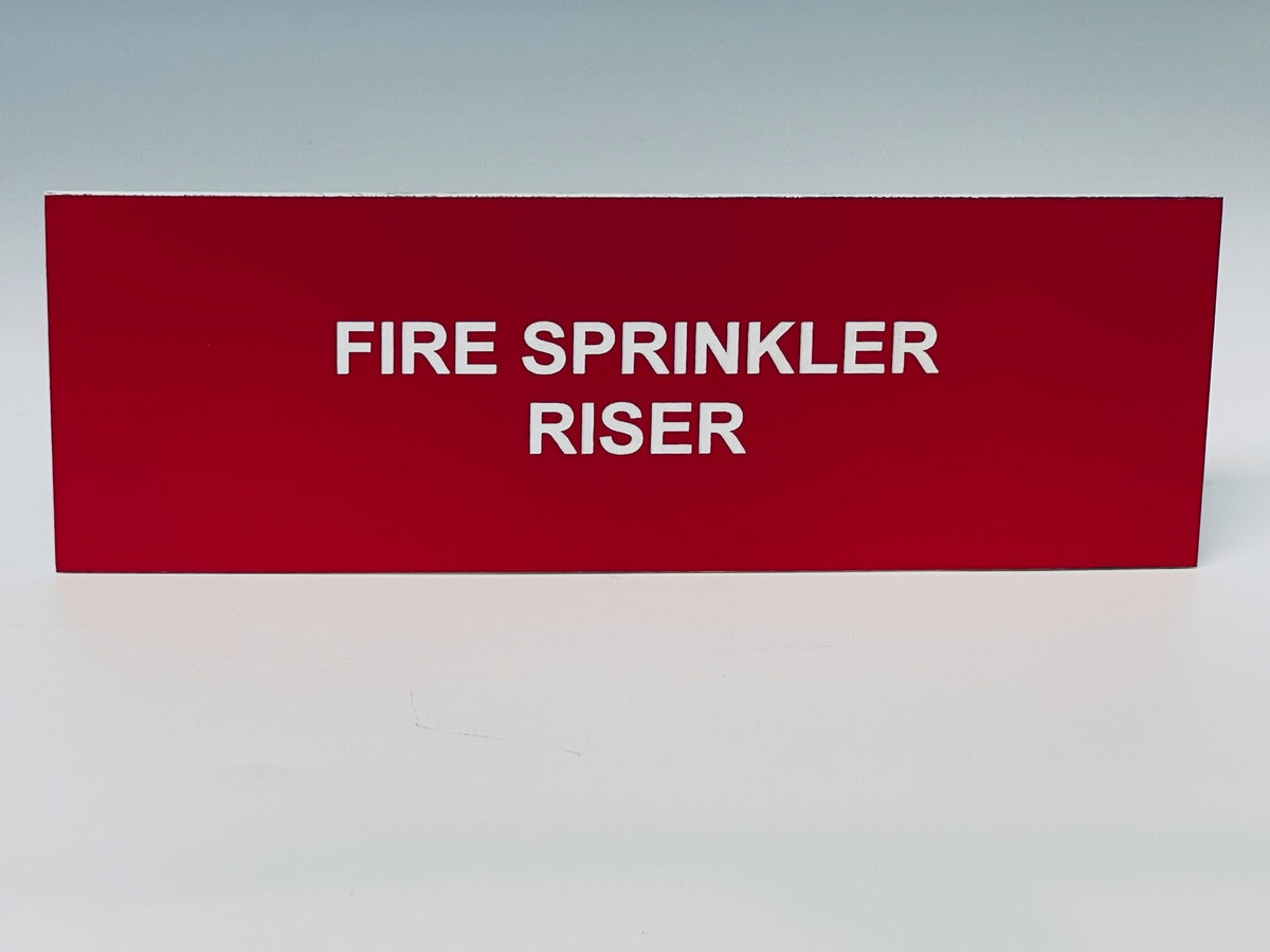 Red engraved placard with white letters reading FIRE SPRINKLER RISER.