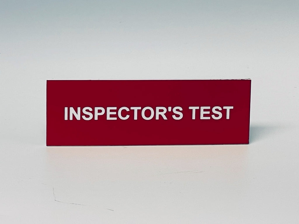 Red engraved placard with white letters reading INSPECTOR'S TEST.