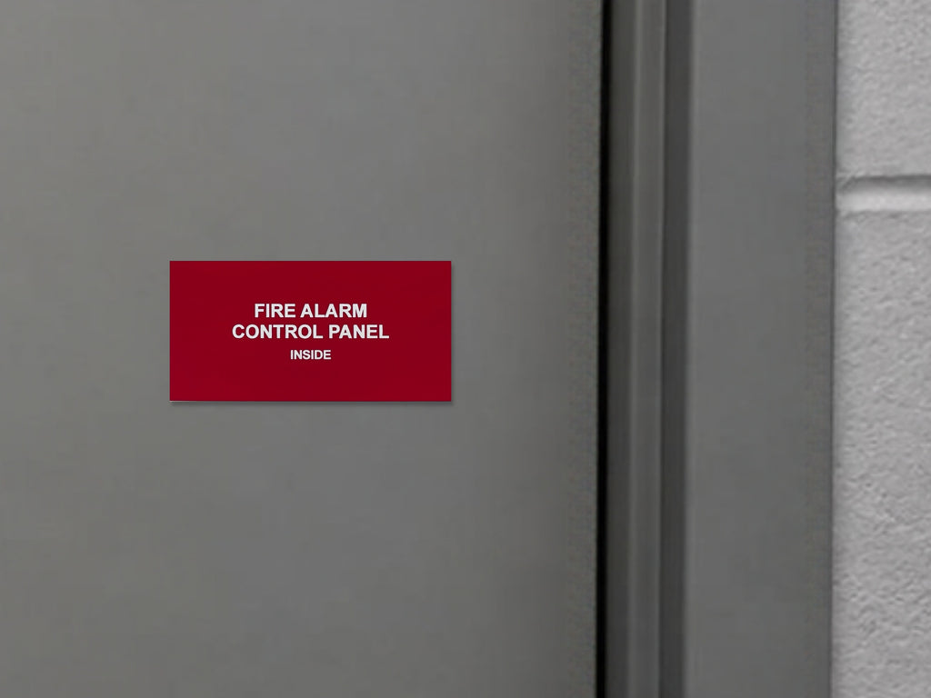 Red engraved FIRE ALARM CONTROL PANEL, INSIDE placard with white letters on a gray steel door beside the door frame.