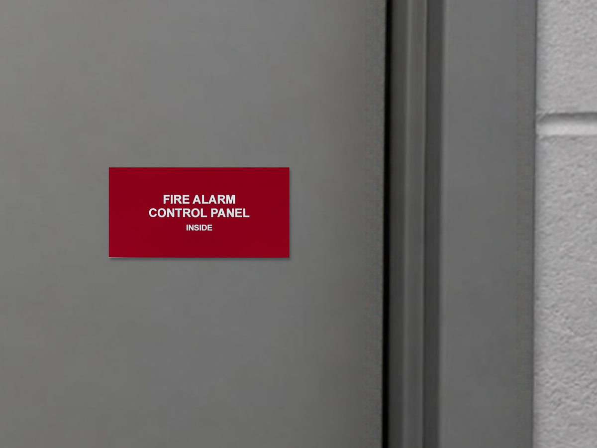 Red engraved FIRE ALARM CONTROL PANEL, INSIDE placard with white letters on a gray steel door beside the door frame.
