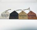 Four house-shaped Christmas ornaments lying in a row on jute twine, each with a cut-out heart: Home Sweet Home, THE GARCIAS, EST. 2026 in linen and walnut finishes, and Our First Home, THE JOHNSONS, 2026 in oak and cherry finishes.