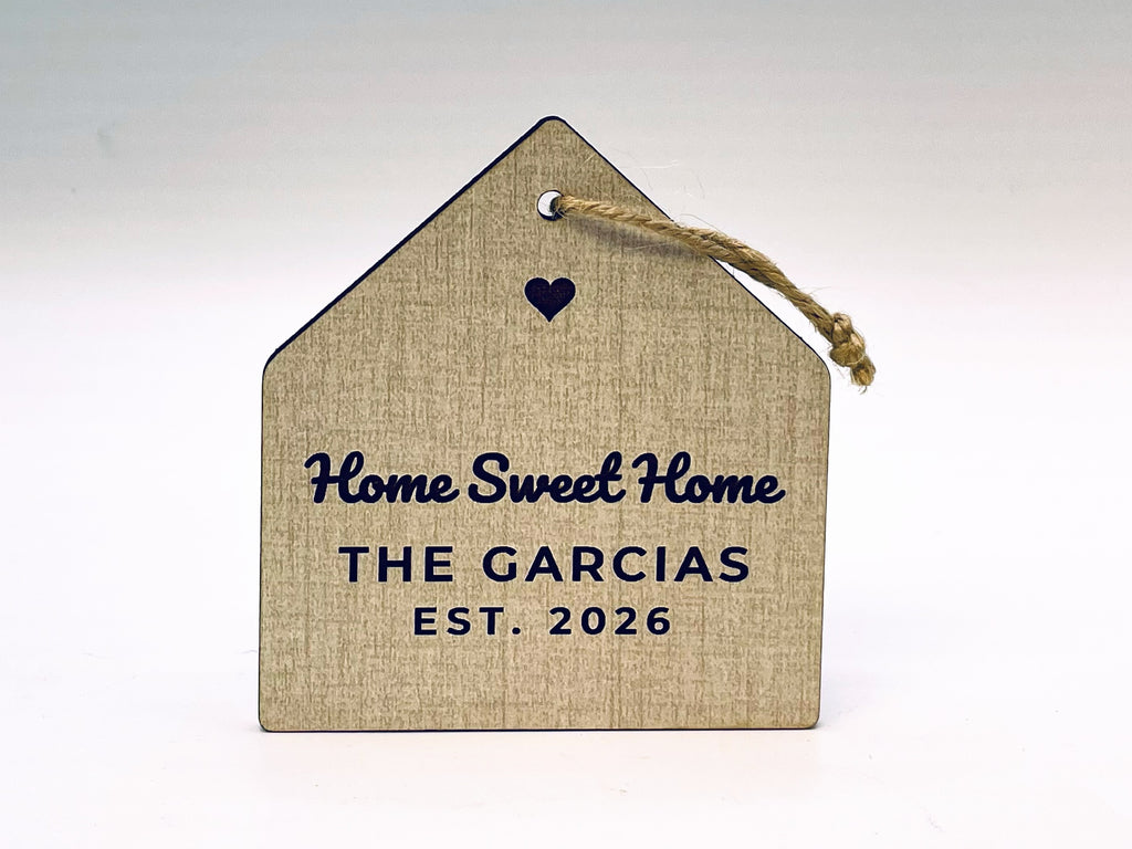 House-shaped ornament in a linen finish on jute twine: a cut-out heart, Home Sweet Home in script, THE GARCIAS and EST. 2026 engraved in black.