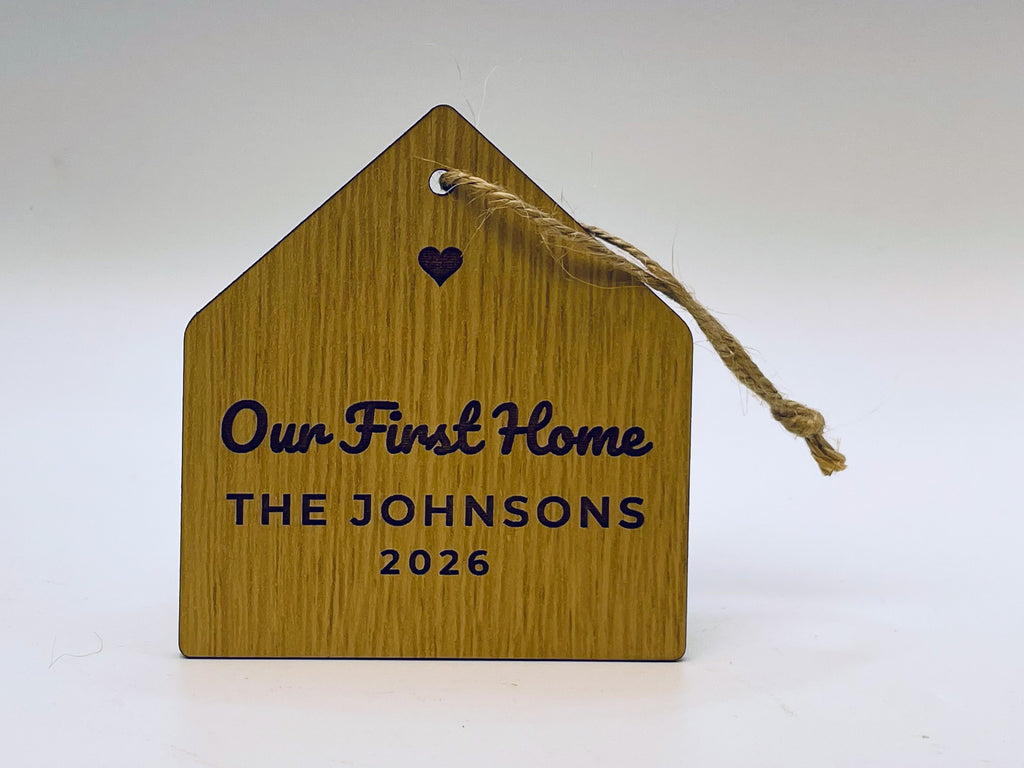 House-shaped ornament in an oak finish on jute twine: a cut-out heart, Our First Home, THE JOHNSONS and 2026.