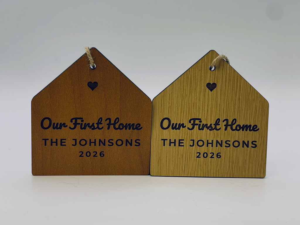 Two Our First Home house ornaments side by side, in cherry and oak finishes.