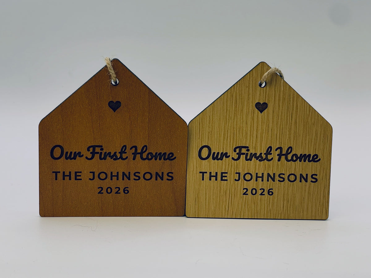 Two Our First Home house ornaments side by side, in cherry and oak finishes.