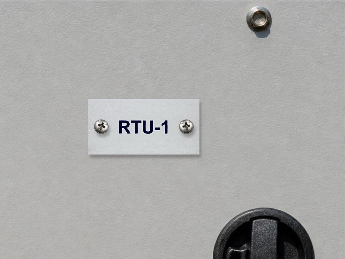 White engraved RTU-1 tag with black letters, screwed to the gray access panel of a rooftop HVAC unit near its latch.