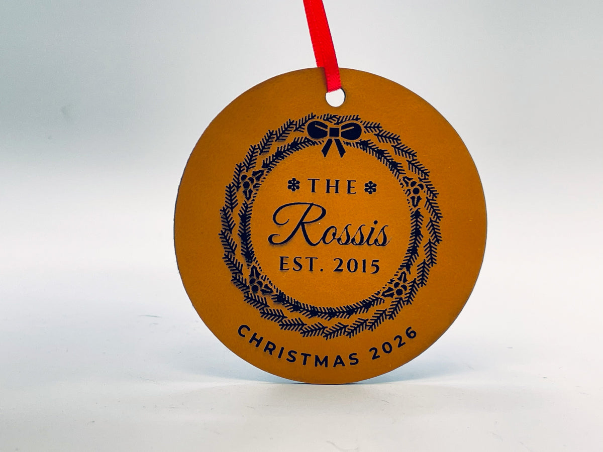 Round rawhide leatherette ornament on red ribbon: THE, Rossis in script and EST. 2015 inside an evergreen wreath with holly and a bow, and CHRISTMAS 2026 along the bottom.