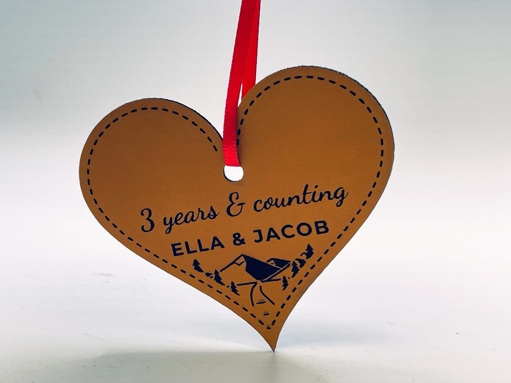 The heart ornament at an angle, showing the leatherette's edge and the engraved mountain scene.
