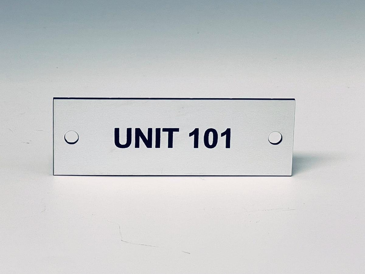 White engraved tag with two screw holes, black letters reading UNIT 101.