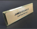 A name badge on a gold metal bar with a brushed metal-look face. JAMES O'CONNOR is engraved in black, with the title Golf Shop Manager in a smaller black font on the line below.