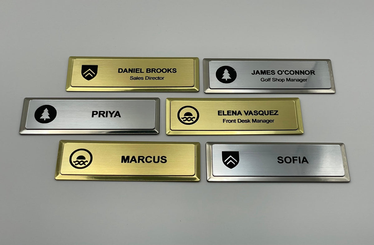 Six premium name badges on gold and silver metal bars, each engraved with a company logo at the left and a name, some with a title.