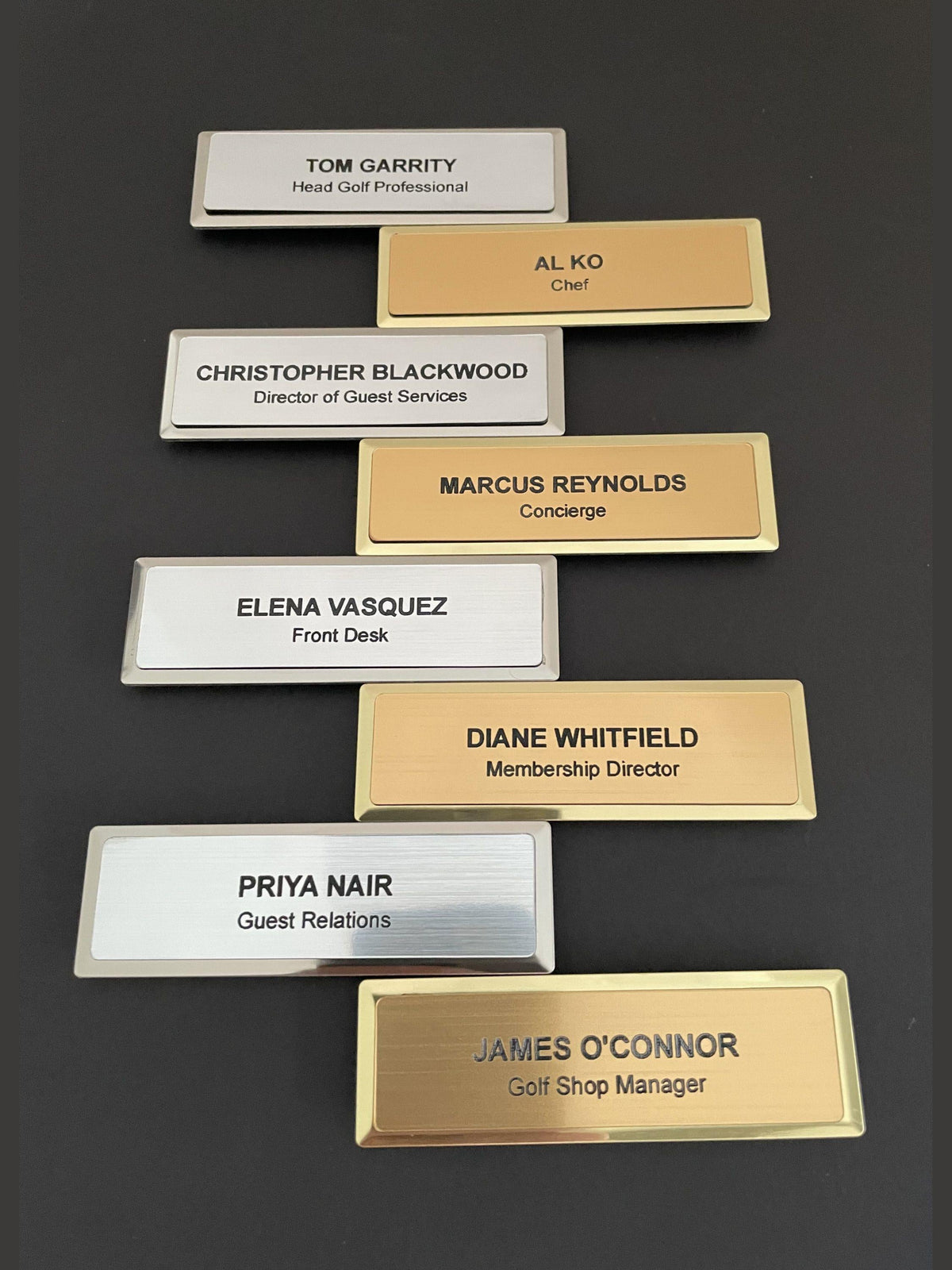 Eight premium name badges, four silver and four gold, each engraved with a name and a job title.