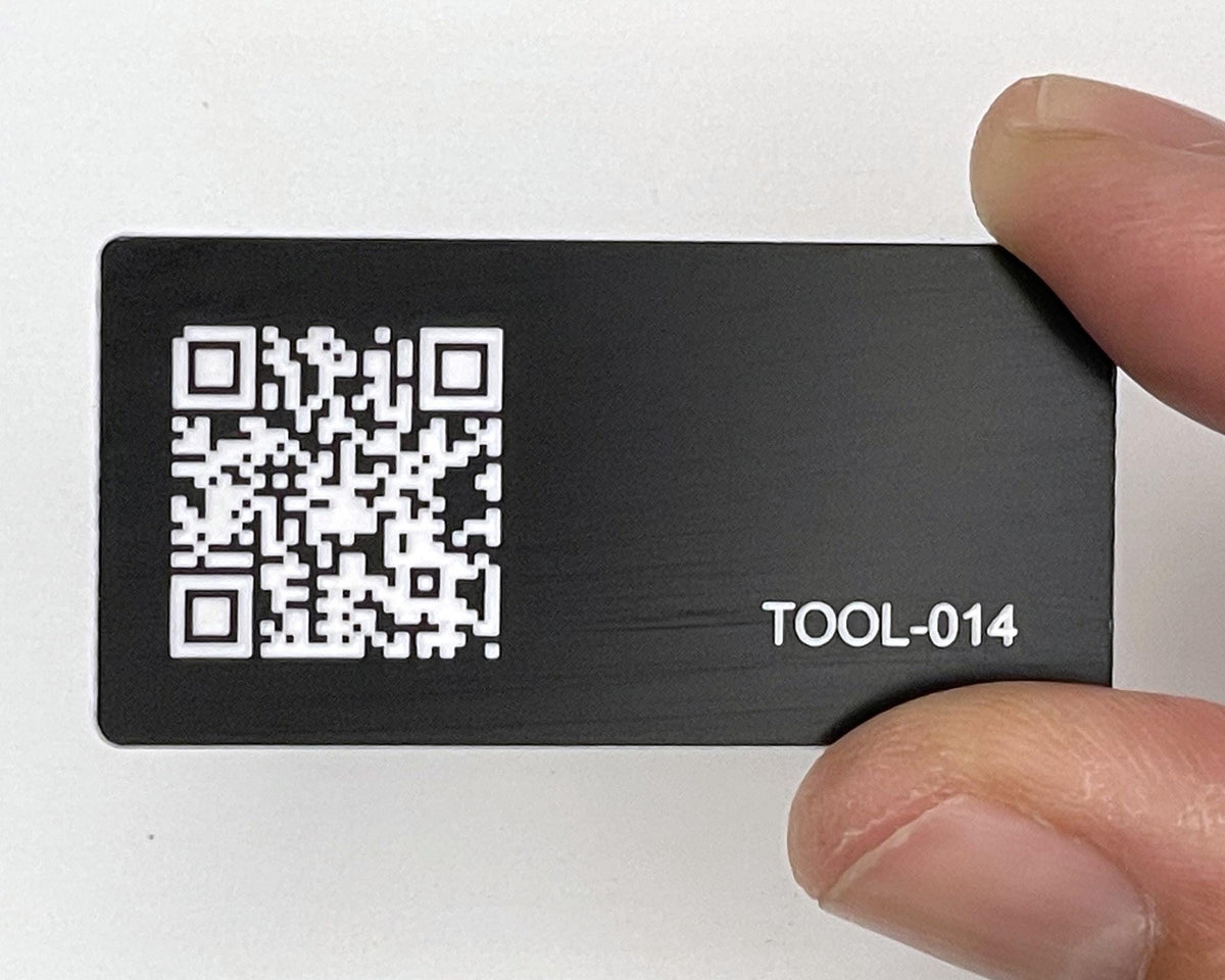 A rectangular black engraved tag featuring a white QR code on the left side and the white text TOOL-014 on the right side. The surface has a smooth matte finish with high contrast white markings for clear visibility.