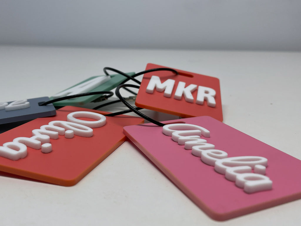 A low, close view of the coral Olivia and pink Amelia tags, showing the white letters standing up off the surface.